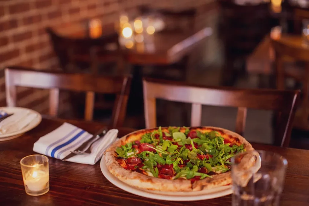 Arugula pizza and candle on a restaurant table.