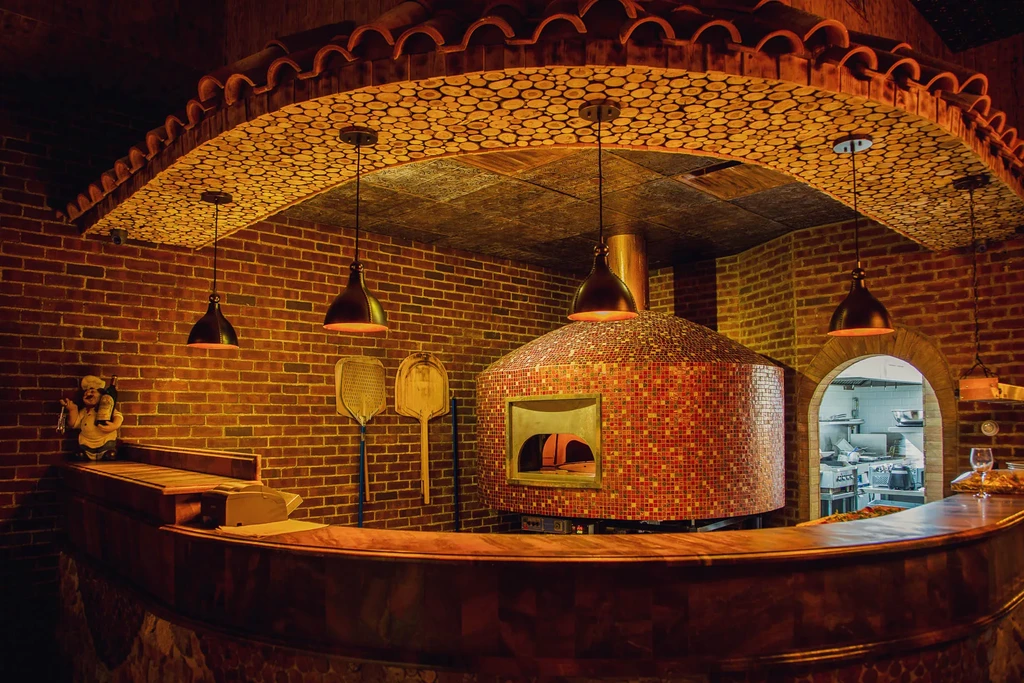Wood-fired pizza oven with mosaic tiles in a brick-walled restaurant.