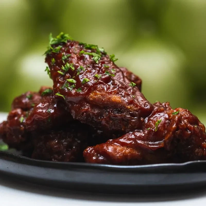 Close-up of BBQ chicken wings with parsley on a black plate.