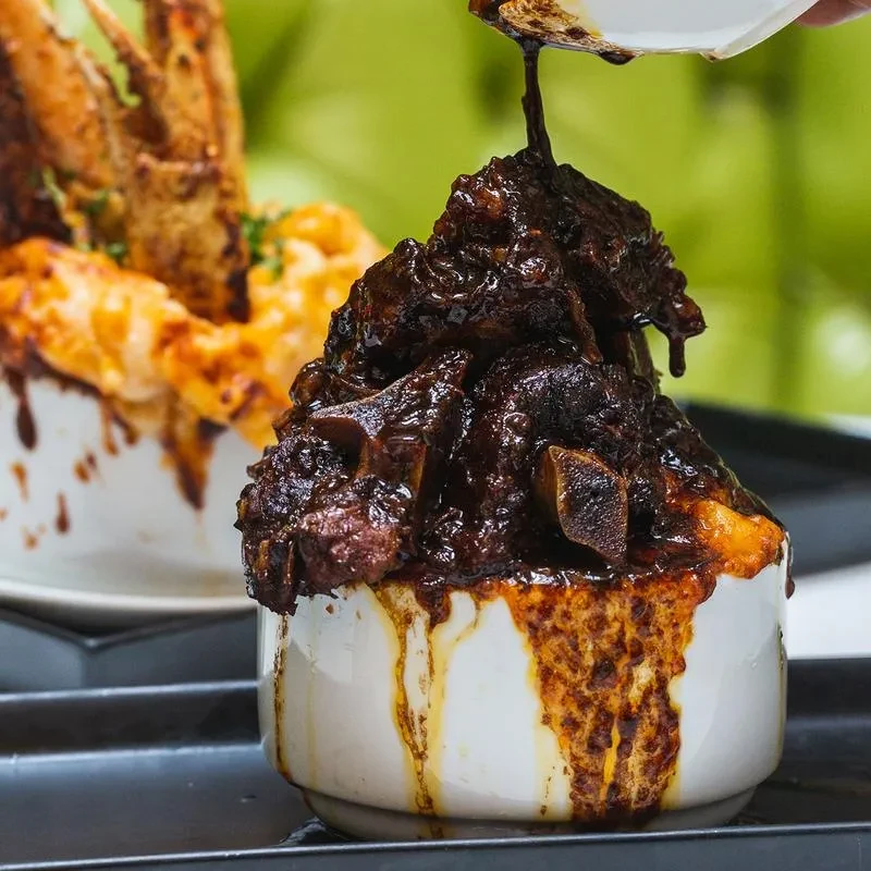 Dark stewed short ribs piled high in a white ramekin, sauce dripping.