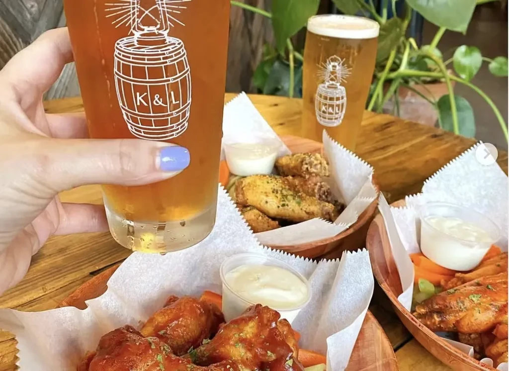 A hand holding a beer glass and baskets of chicken wings on a table.