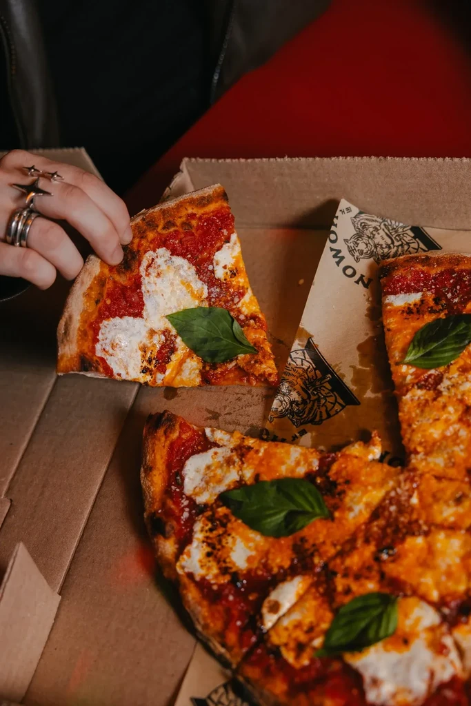 A hand picking up a slice of pizza from a box.