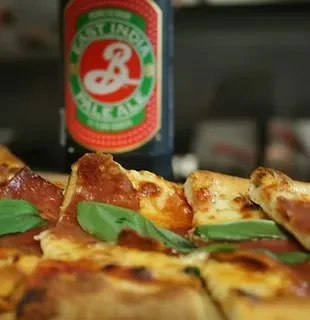 A bottle of East India Pale Ale next to slices of pizza.