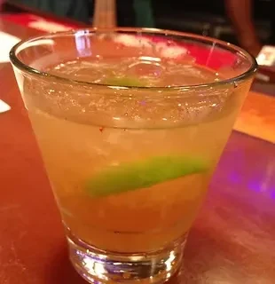 A short glass of iced amber liquid with two lime wedges.