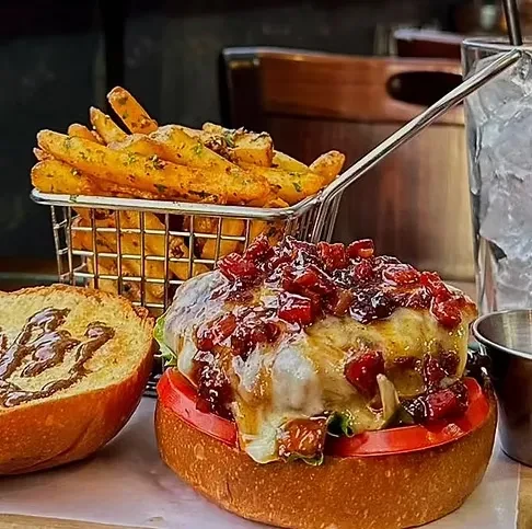 A gourmet burger with bacon jam and cheese, fries, and iced drink.