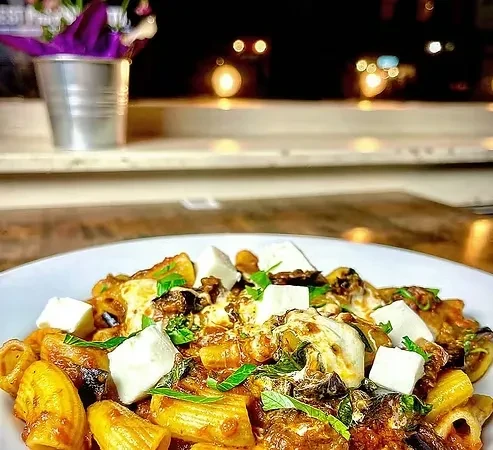 A bowl of rigatoni pasta with cubed cheese, basil, and sauce.