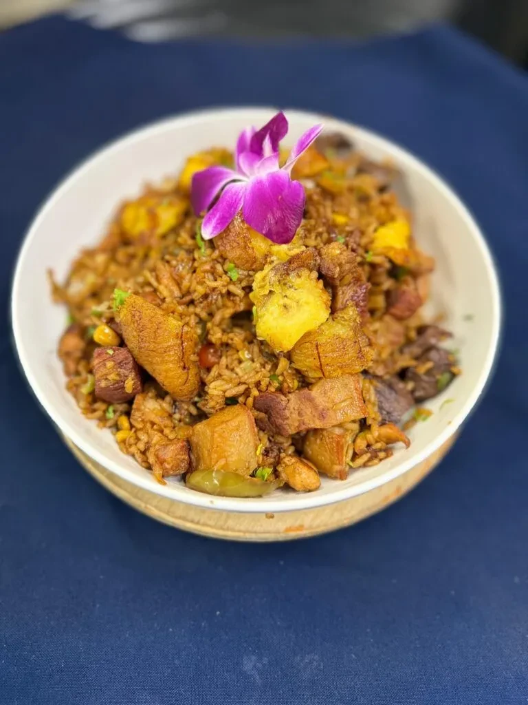 Fried rice with pork, plantains, and a purple orchid garnish in a bowl.