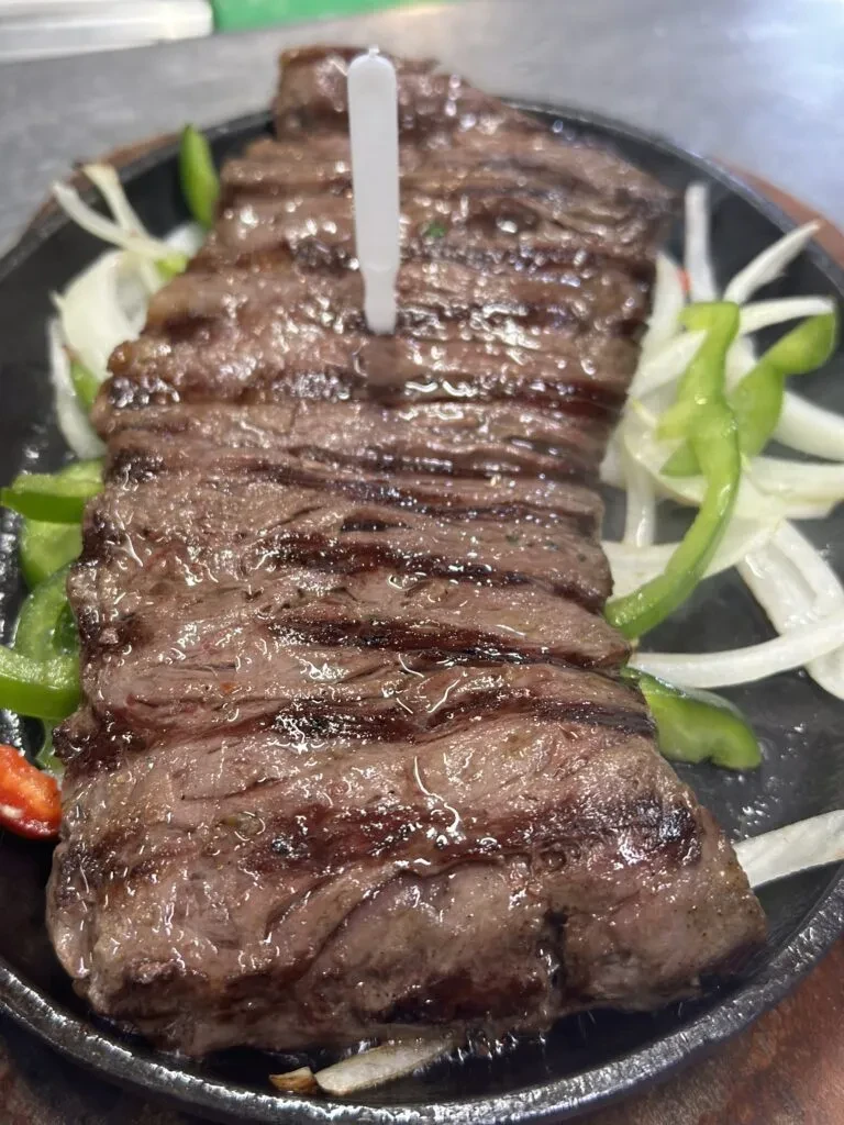 Sizzling steak strips with onions and peppers on a black platter.