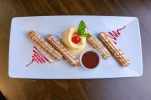 Churros, ice cream with cherry, and chocolate sauce on a white plate.