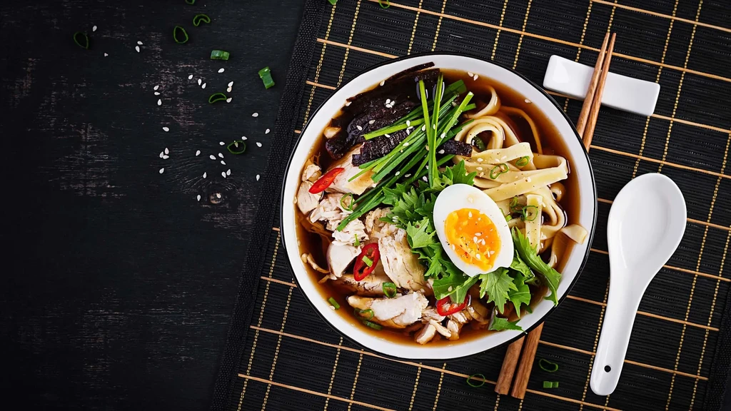 A bowl of chicken ramen with egg, greens, and chopsticks.