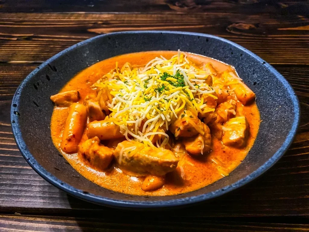 A blue bowl of chicken and rice cakes with cheese and parsley.