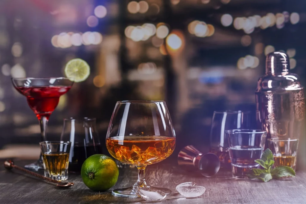 Various cocktails, limes, and bar tools on a wooden table.