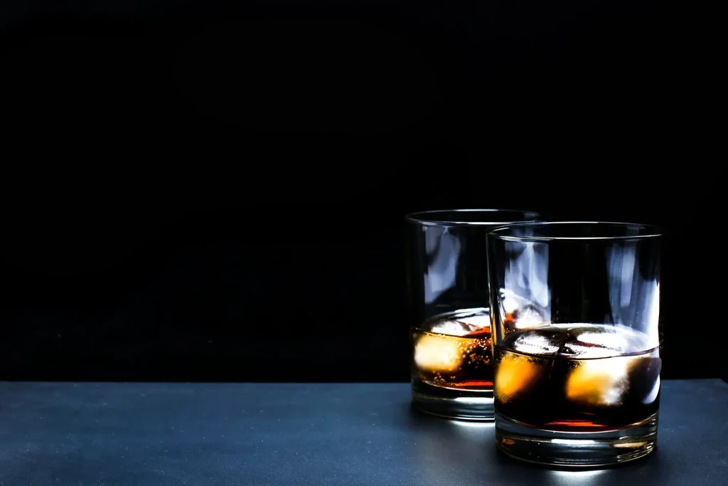 Two glasses of whiskey on a black background with ice.