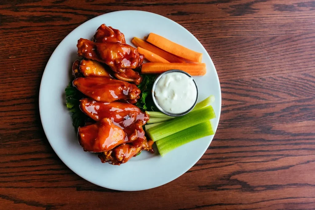 A plate of buffalo wings, carrots, celery, and dip on a wooden table.