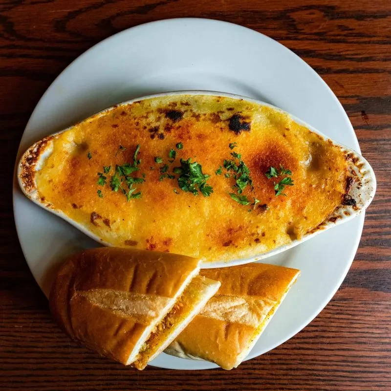 A baked casserole with bread rolls on a white plate.