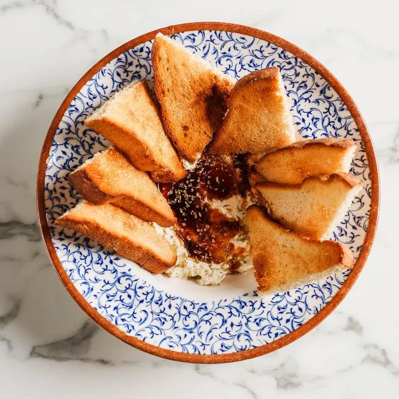 Toasted bread triangles with white dip and jam on a patterned plate.