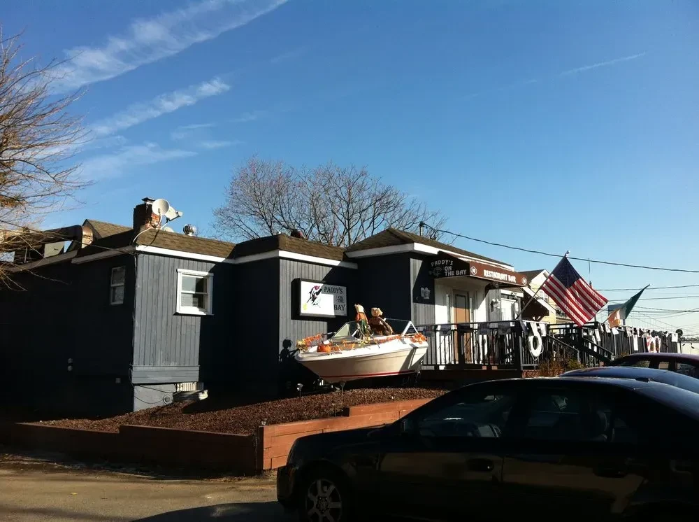 "Paddy's on the Bay" restaurant with a boat display and American flag.