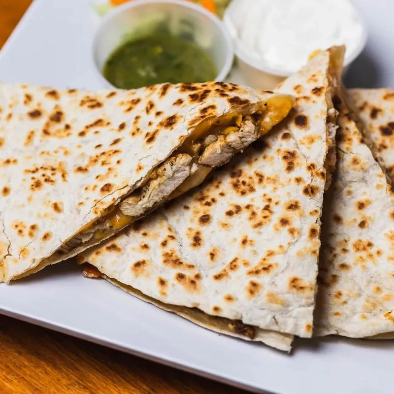 Chicken quesadilla slices with green salsa and sour cream.