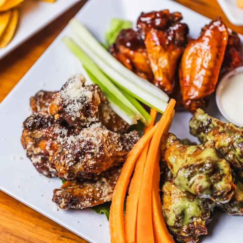 A plate of three varieties of chicken wings with celery and carrot sticks.