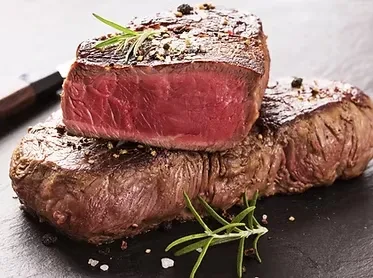 Two medium-rare steaks seasoned with pepper, salt, and rosemary sprigs.