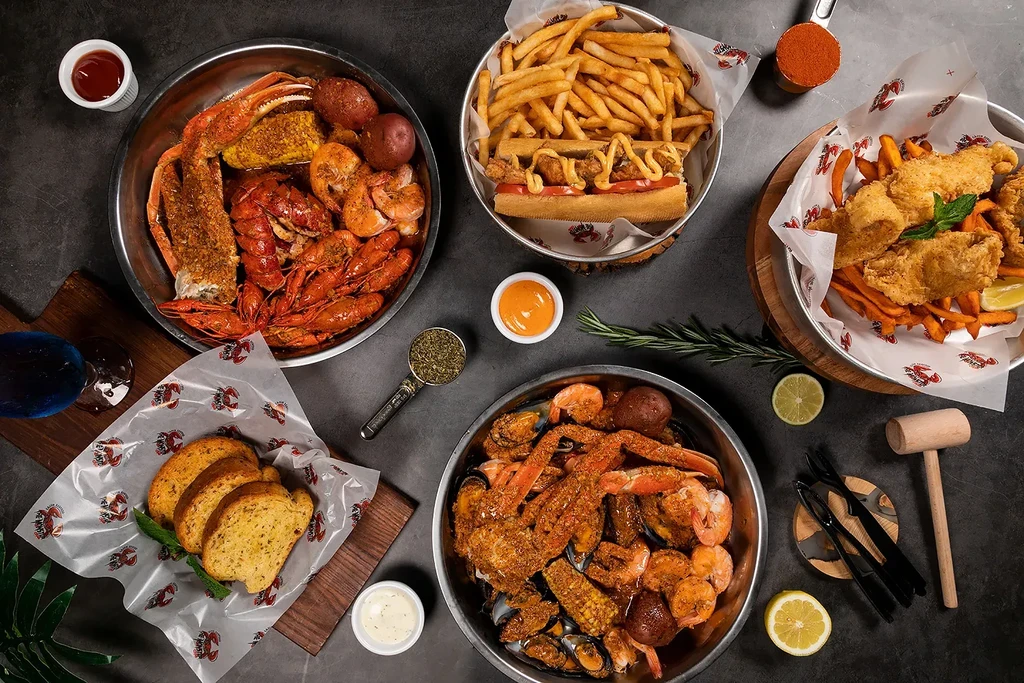 Overhead shot of seafood boils, fries, sandwich, and bread on a table.