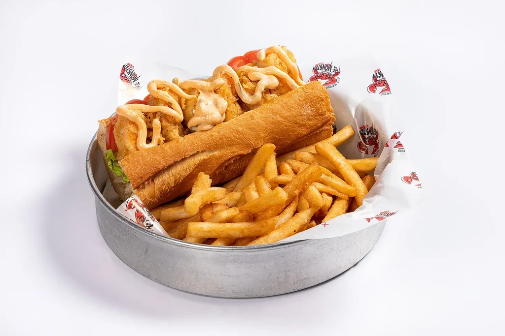 A fried shrimp po'boy with fries, served in a metal bowl.
