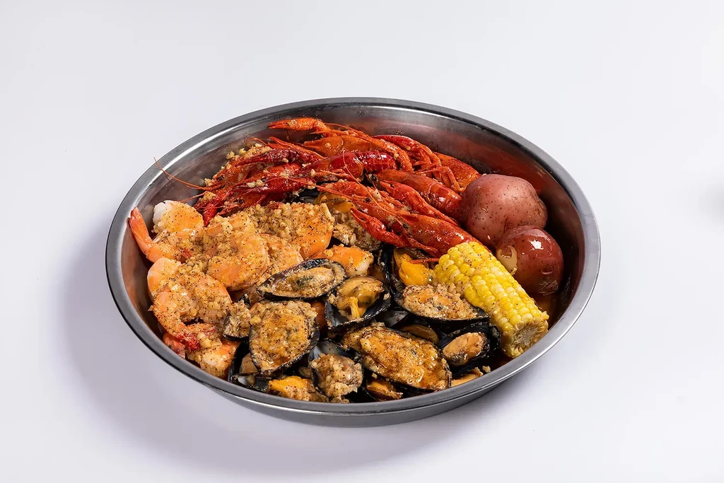 A metal bowl filled with shrimp, crawfish, mussels, corn, and potatoes.