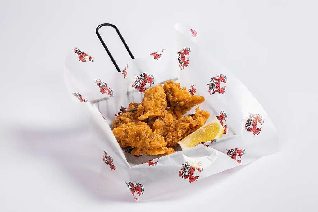 Fried seafood in a basket with a lemon slice on white paper.