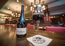 A wine bottle and glass on a bar counter in a restaurant.
