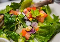 A close-up of a green salad with corn, tomatoes, and red onion.