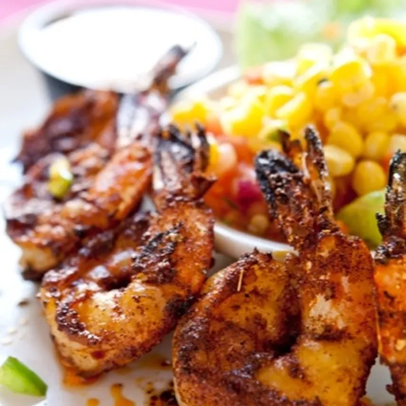 Grilled shrimp with corn salsa and a side of white sauce.
