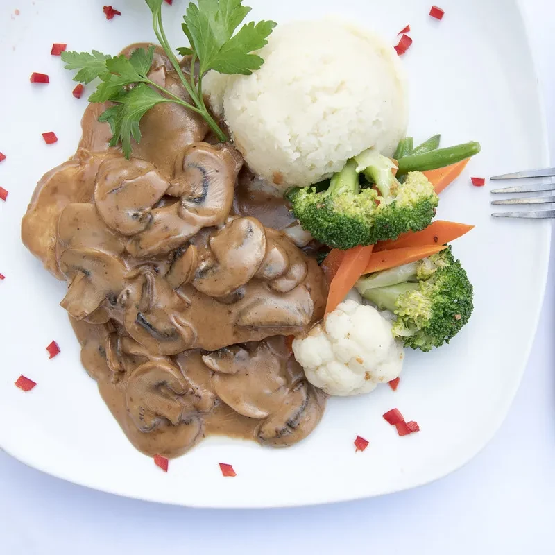 Mushroom in brown sauce, mashed potatoes, and steamed vegetables on a plate.