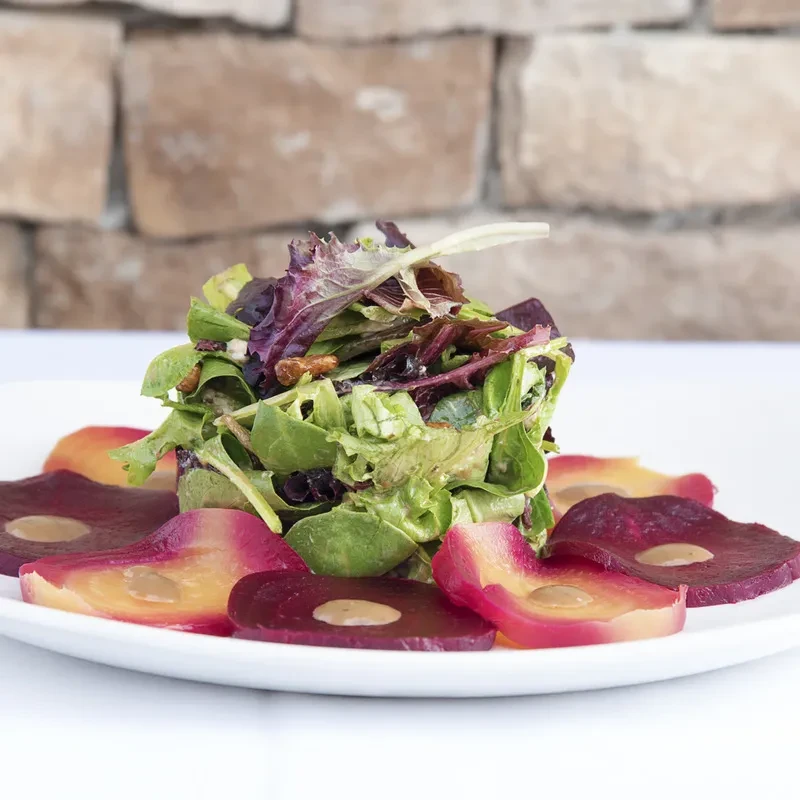 A salad with greens, pecans, and sliced beets with dressing.