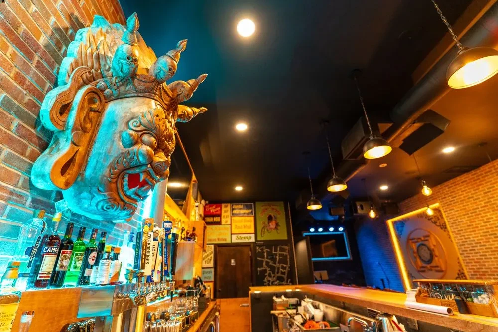 Large carved head sculpture overlooks a bar with drinks and beer taps.