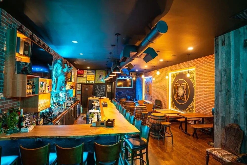 Bar interior with long counter, brick walls, and contrasting lighting.