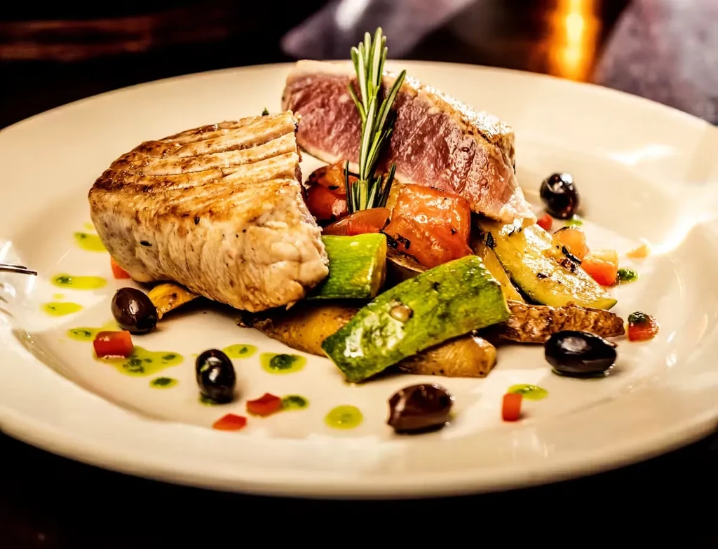 A plate of seared tuna, roasted vegetables, olives, and rosemary.