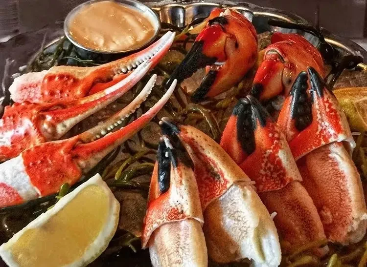 A platter of cooked crab legs and claws with dipping sauce and lemon.