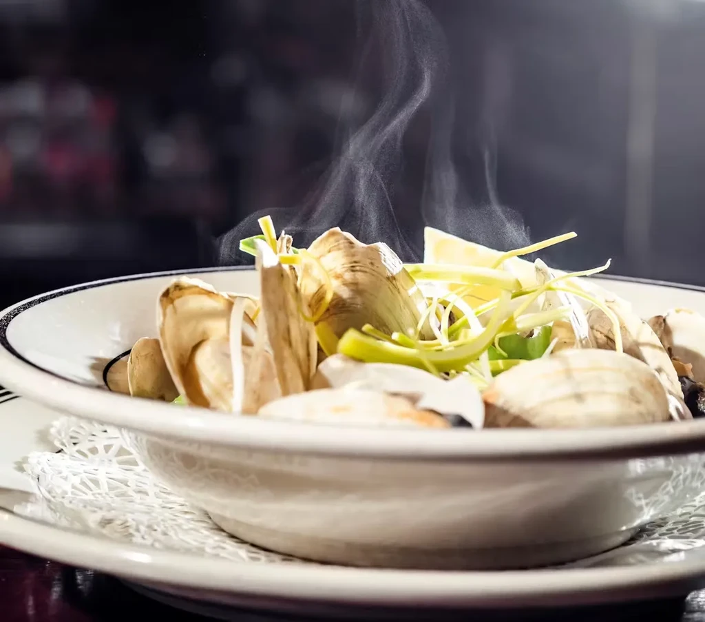 Steaming hot bowl of clams with sliced leeks and lemon.