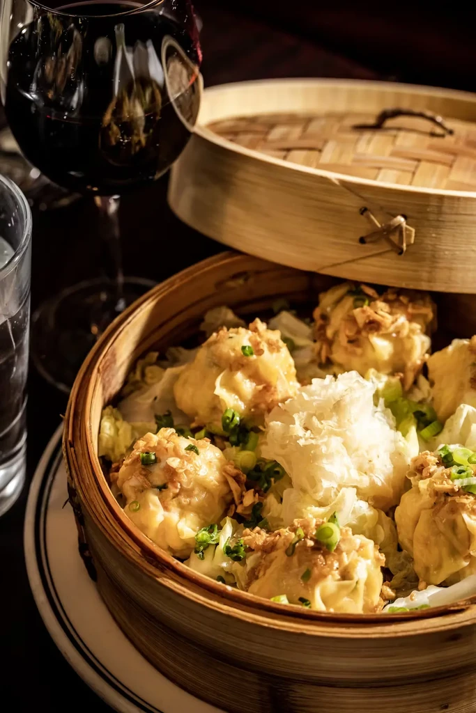 Dim sum dumplings in a bamboo steamer with red wine.