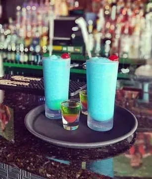 Two blue frozen drinks and two colorful shots on a tray at a bar.