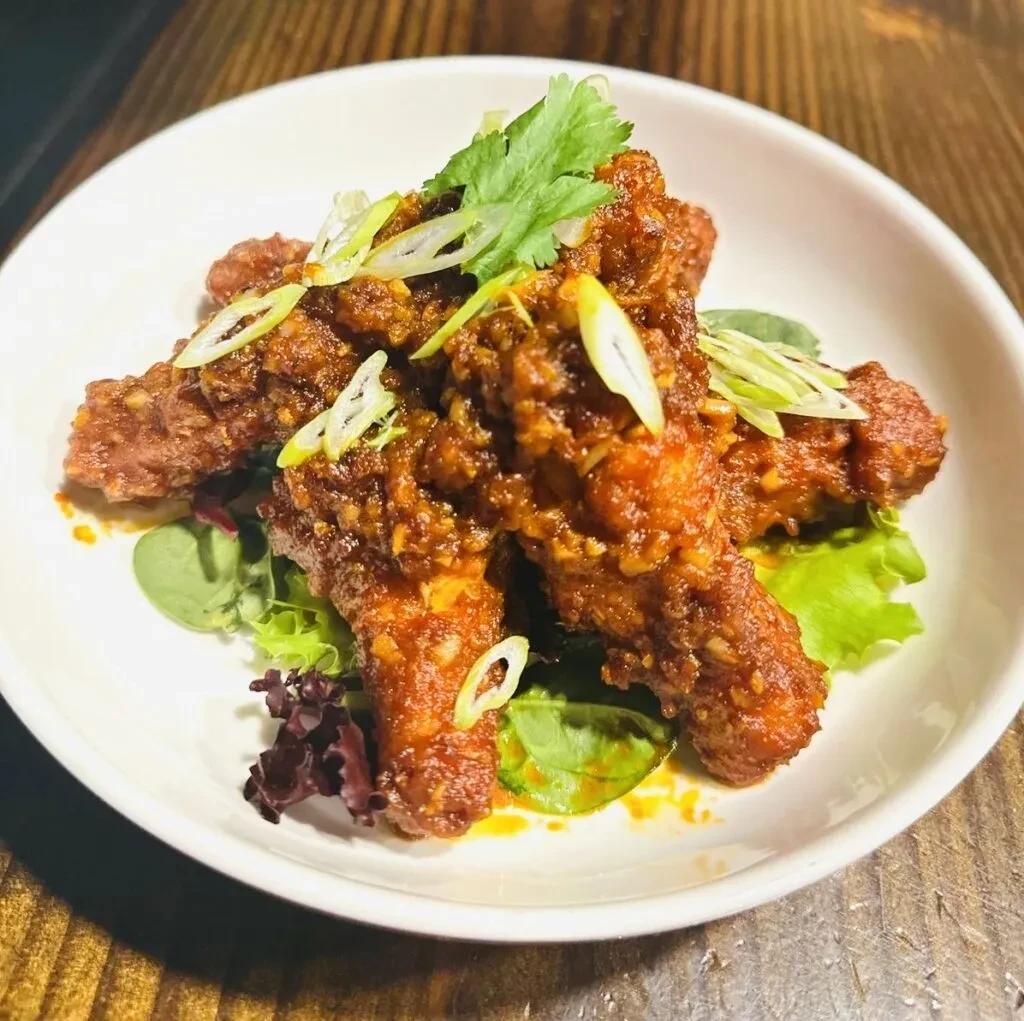 Chicken wings in sauce with garnishes on a white plate.