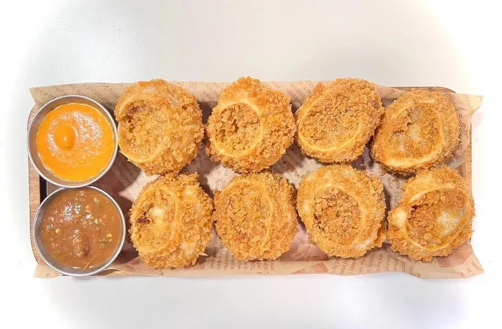 Eight fried breaded onion rings and two dipping sauces on a wooden board.