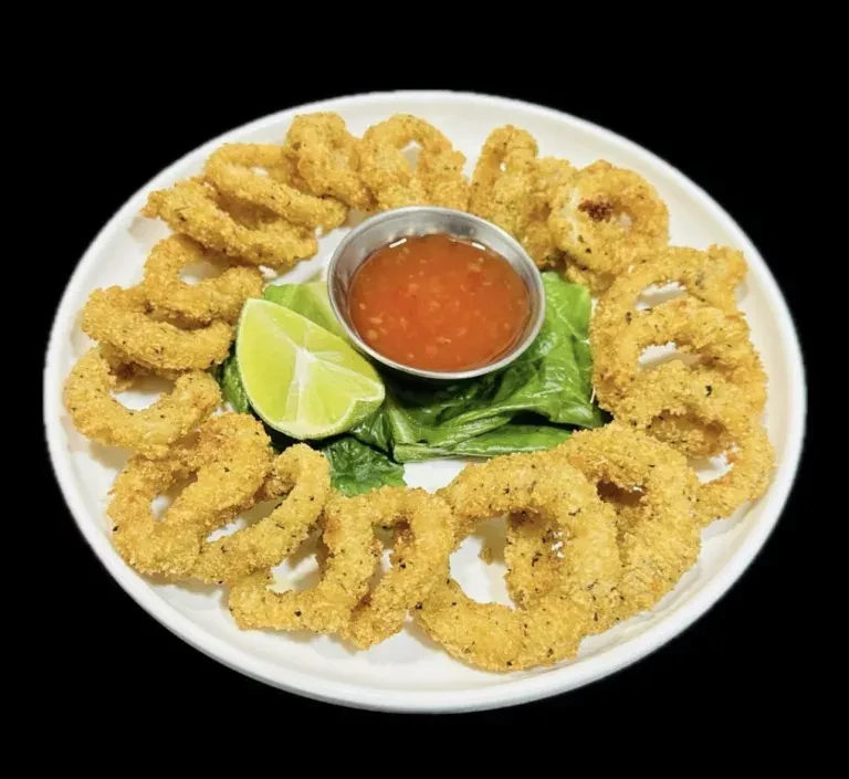 A plate of breaded onion rings with sauce, lime, and lettuce.