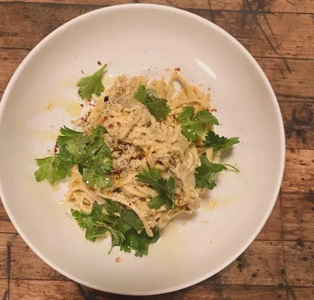 Pasta with creamy sauce, fresh herbs, and spices in a white bowl.