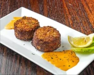 Two fried patties on white plate with lemon and orange sauce.