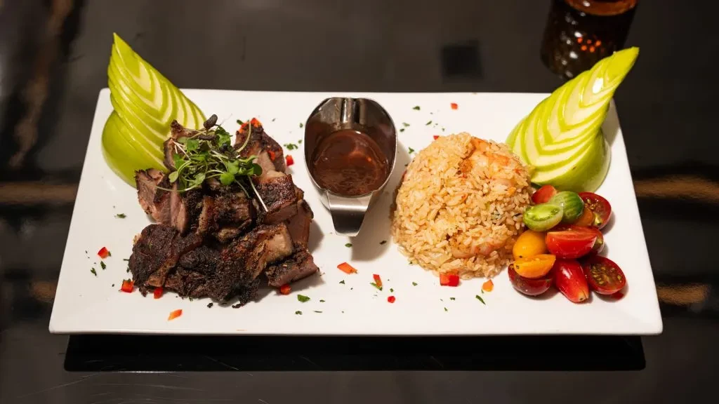 Grilled pork with rice, tomatoes, sauce, and carved green apples on a plate.