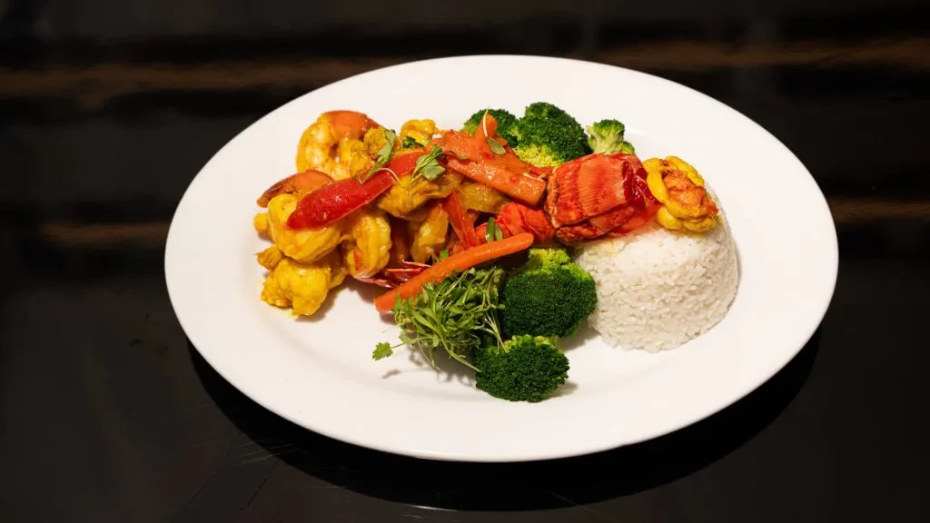A white plate of curry lobster and shrimp with rice and broccoli.
