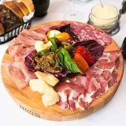 A charcuterie board with sliced meats, cheese, and roasted vegetables.