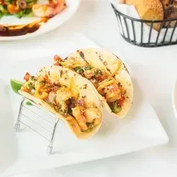 Two grilled shrimp tacos with lime on a white plate.