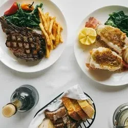 Two plates of food, a bottle of wine, and a breadbasket.